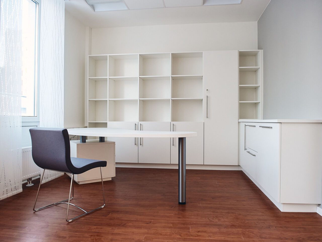 Modernes B&uuml;ro mit wei&szlig;en Regalen, Schreibtisch, schwarzem Stuhl und Holzboden.