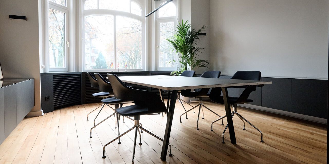 Modernes B&uuml;ro mit schwarzem Schreibtisch, vier St&uuml;hlen und gro&szlig;en Fenstern zur Naturbelichtung.