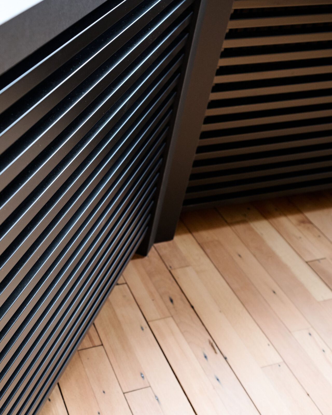 Schwarze Lamellenwand neben Holzboden in moderner B&uuml;roeinrichtung.