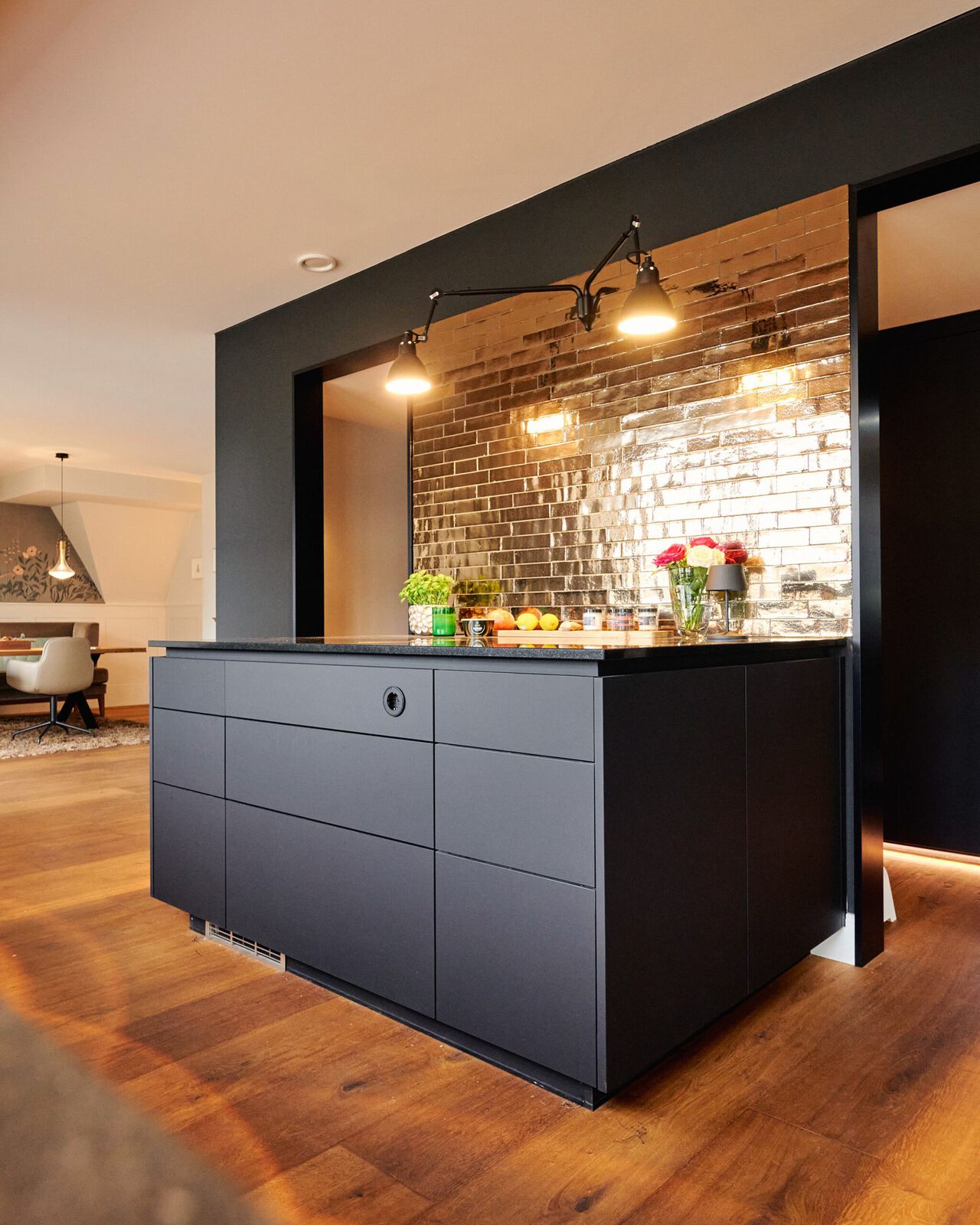 Moderne schwarze Küchenbar mit Holzoberfläche, Backsteinrückwand und hängenden Pendelleuchten in hellem Wohnraum.
