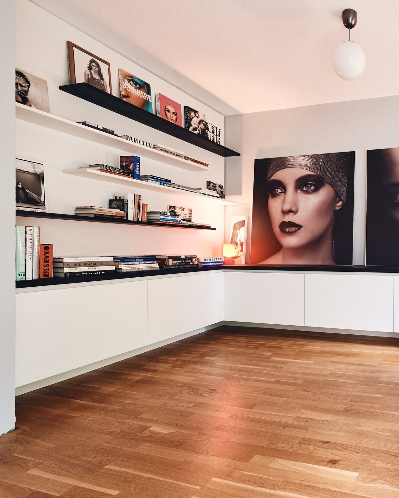 Modernes Wohnzimmer mit weißen Unterschränken, schwarzen Wandregalen und Holzboden.