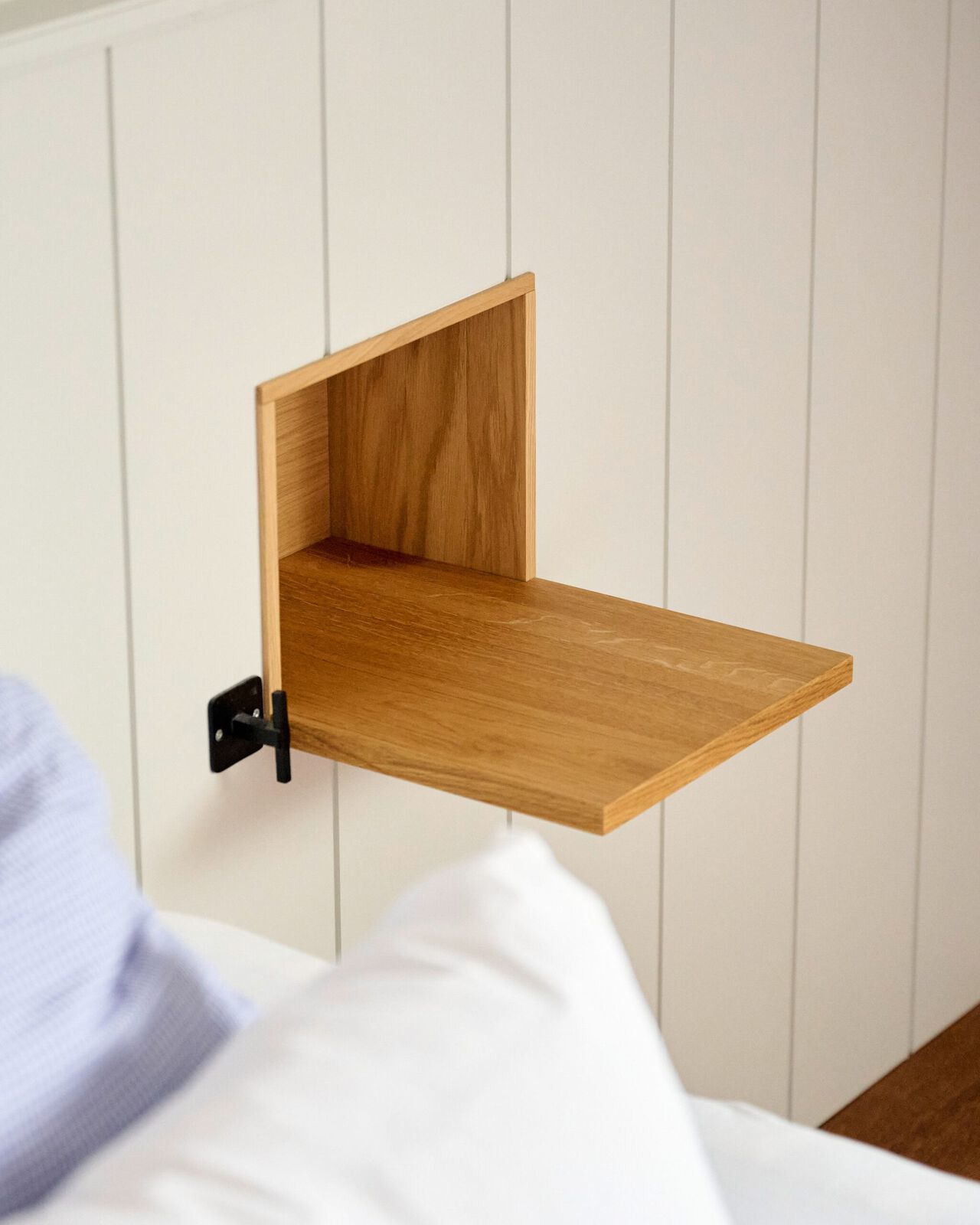 Holzklapptisch aus hellem Holz, an weißer Wand montiert, mit schwarzem Metallhalter.