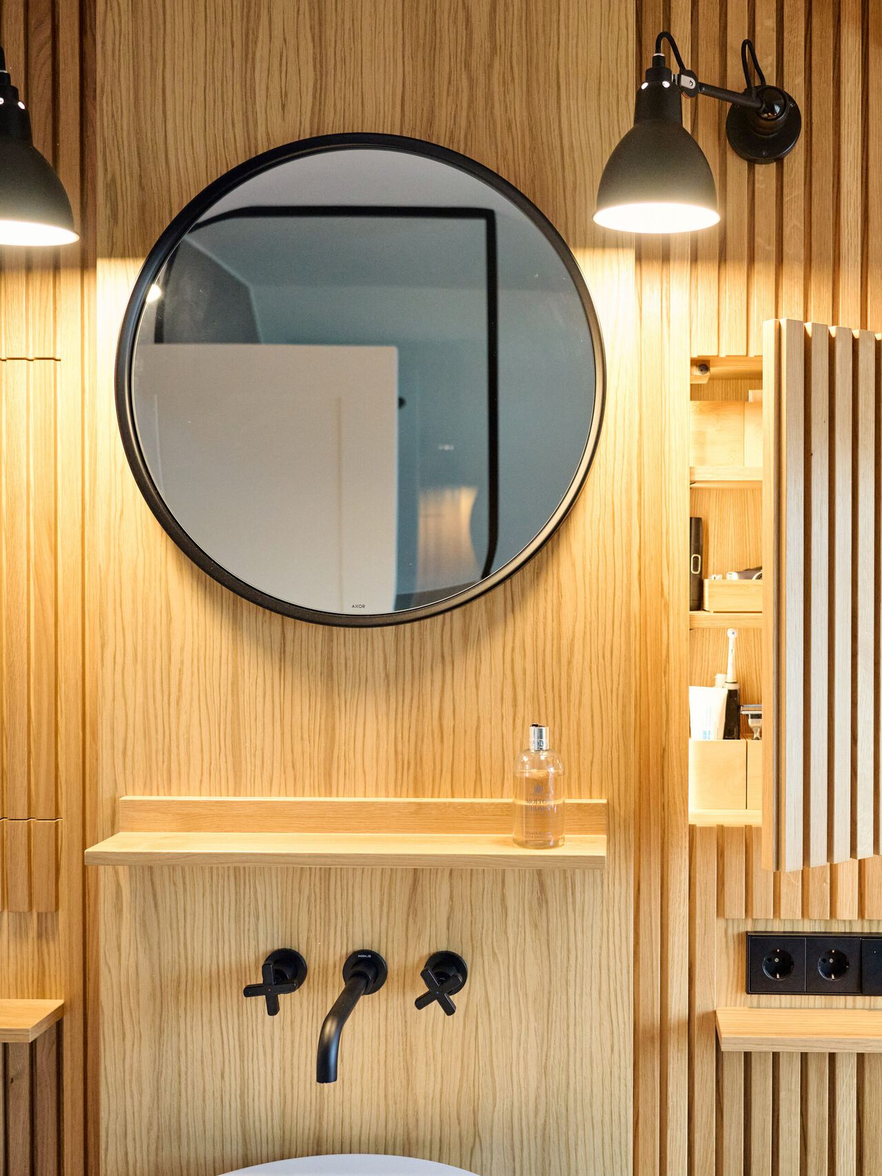 Modernes Badezimmer mit runder schwarzer Spiegeln, Holzverkleidung und schwarzen Wandarmaturen.