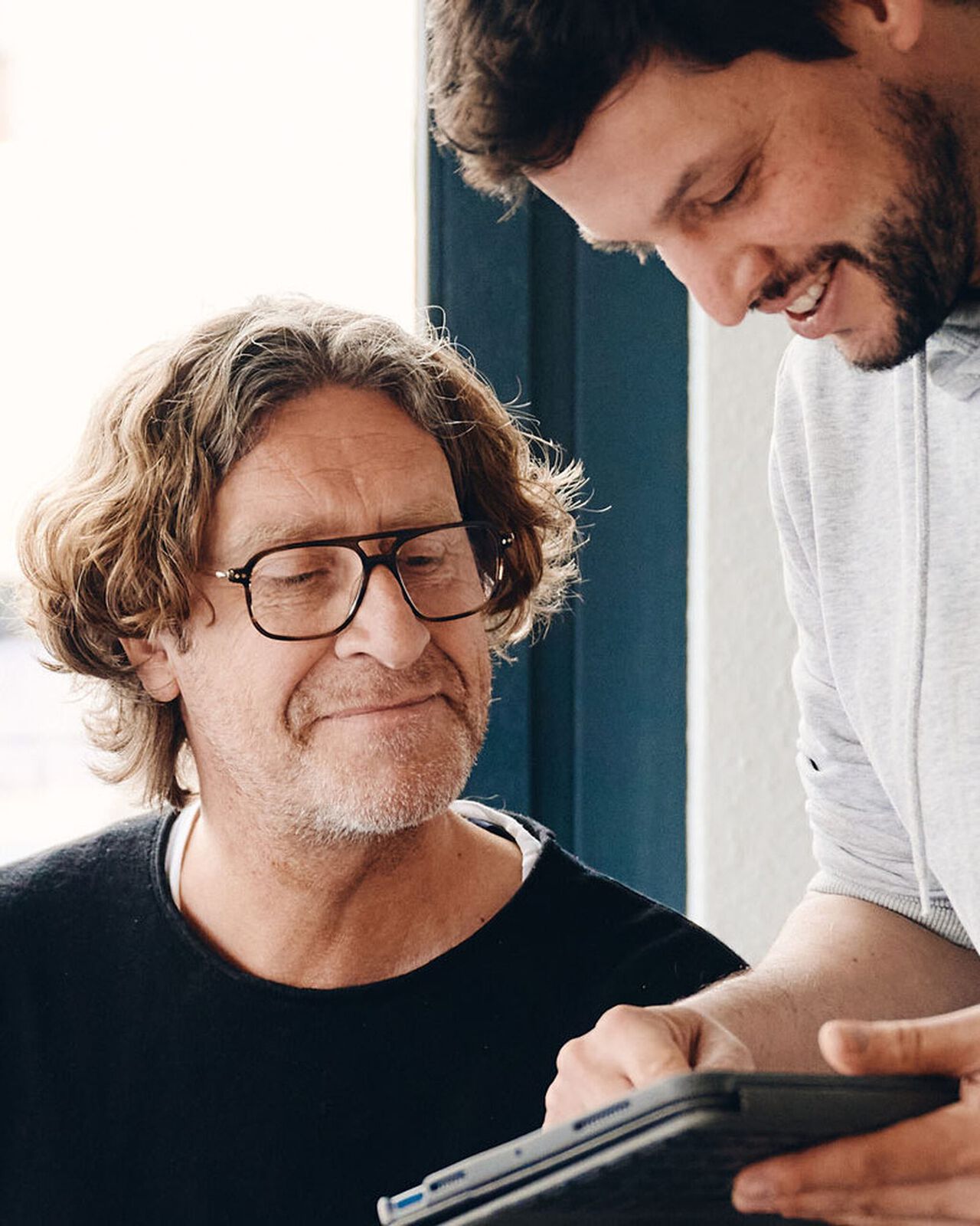 Marc und Butsch schauen gemeinsam auf ein Tablet. Ein Mann mit Brille sitzt, der andere steht neben ihm und zeigt auf das Ger&auml;t.