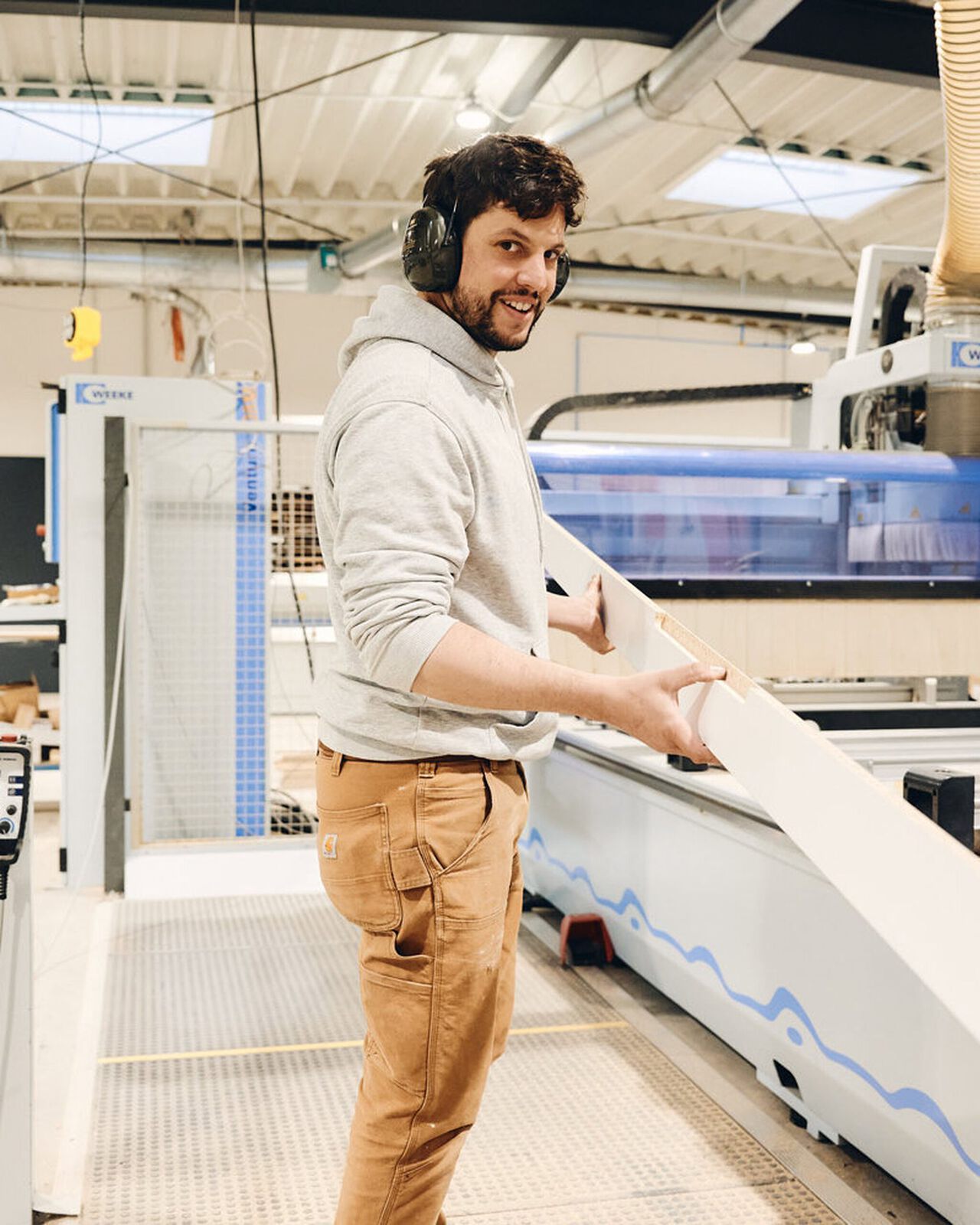 Butsch mit Geh&ouml;rschutz bedient eine gro&szlig;e Holzbearbeitungsmaschine in einer Werkstatt.