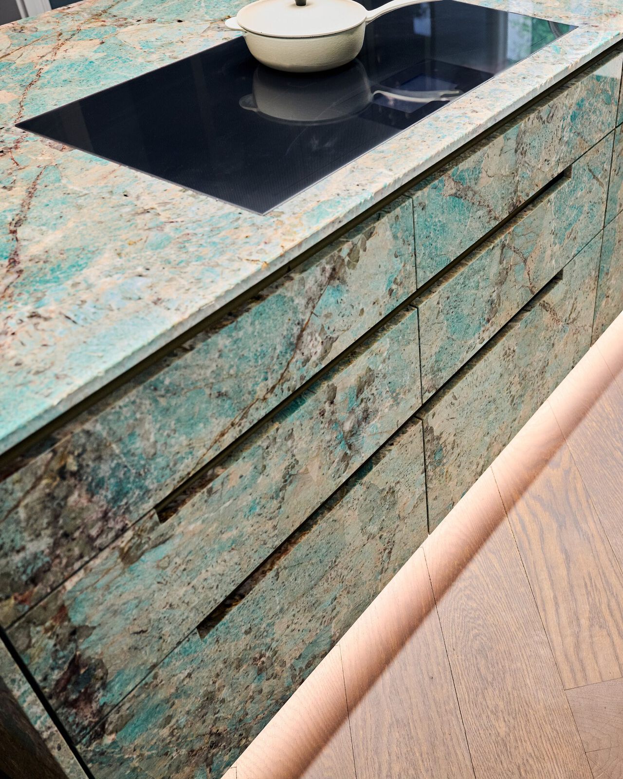 Moderne Küchenfront mit Türkis-Patina-Optik und schwarzer Kochplatte mit weißem Topf.