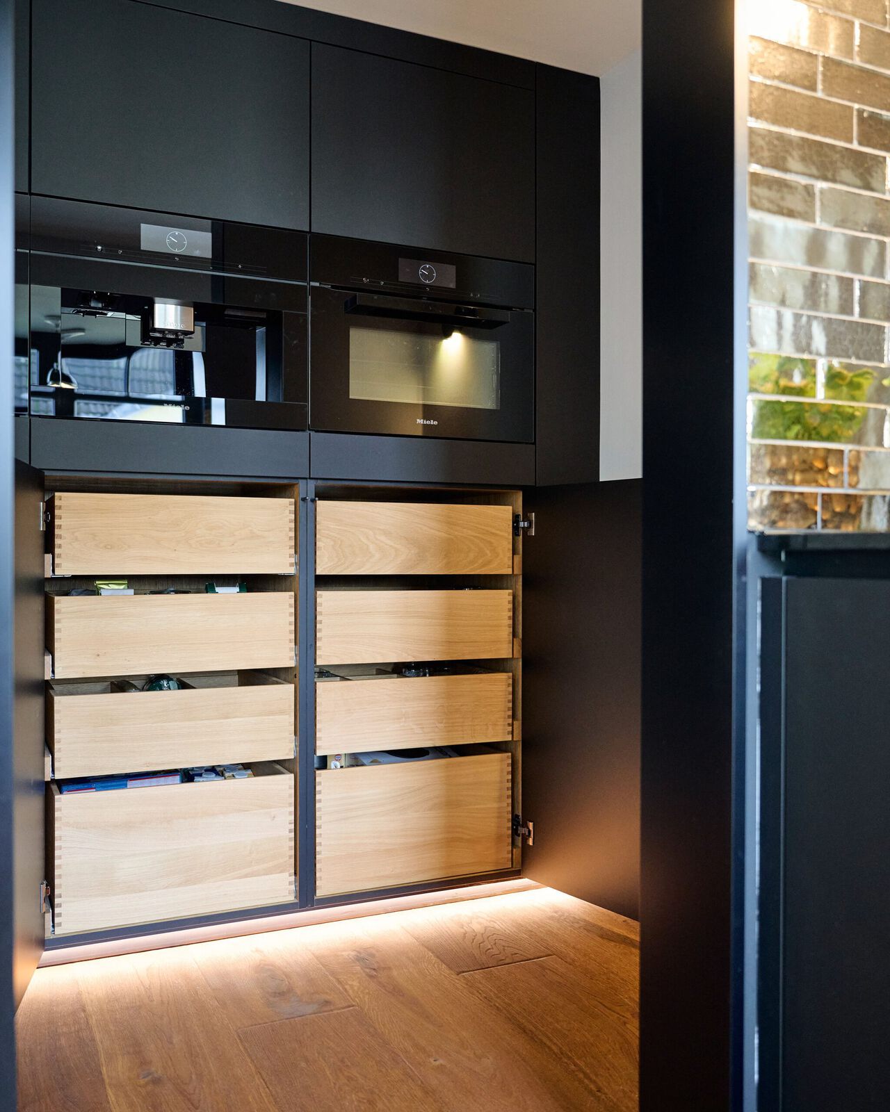 Moderne schwarze Küche mit offenen Holzschubladen und integrierten Elektrogeräten.