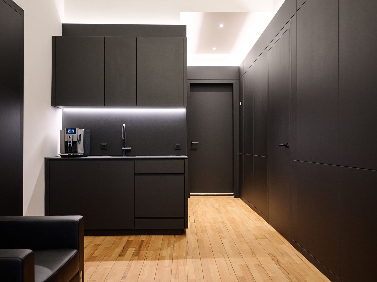 Moderne Küche mit schwarzen Fronten, LED-Beleuchtung und Holzboden in minimalistischem Design.