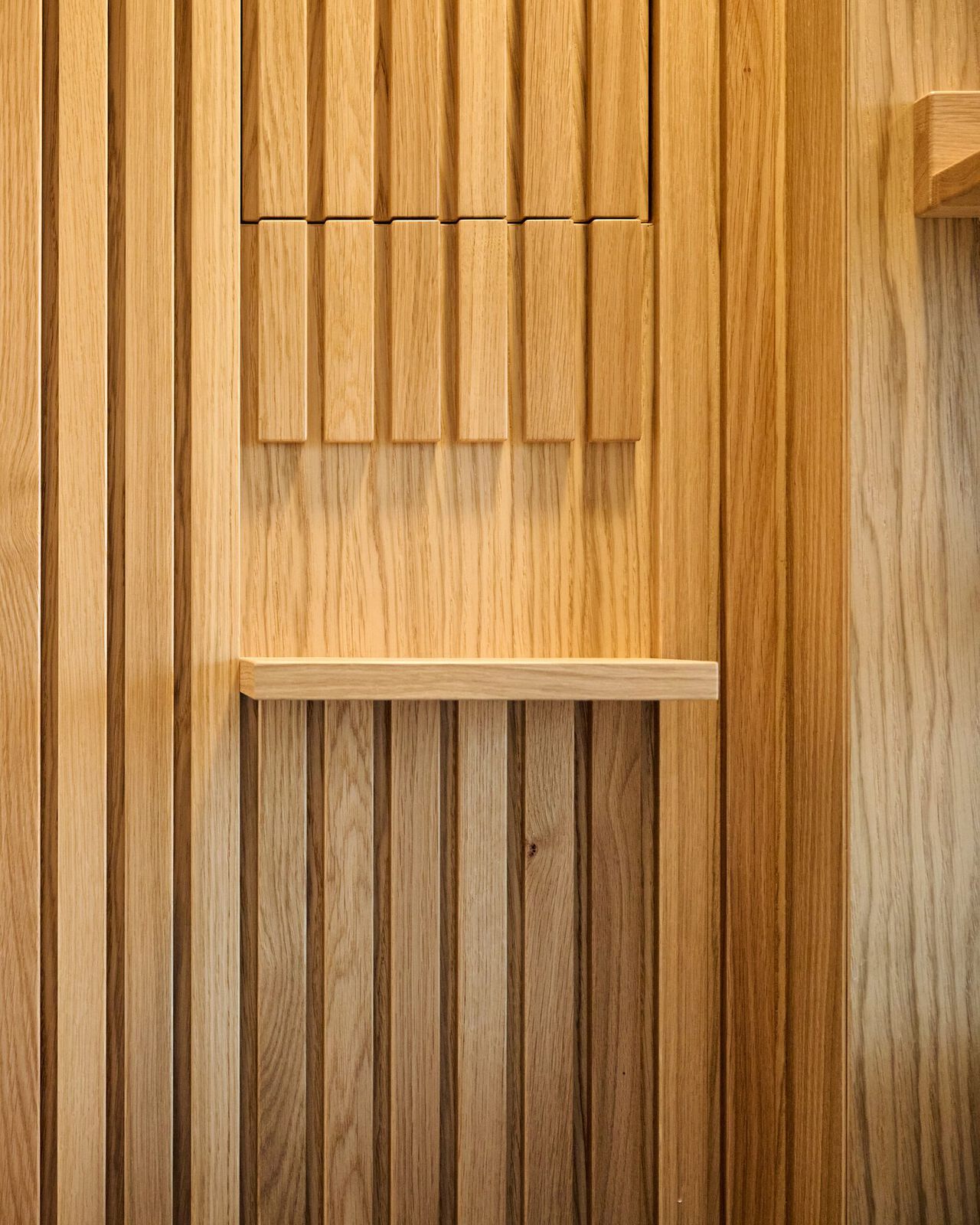 Holzwand mit vertikalen Lamellen und zwei integrierten Regalen in heller Eichenoptik.