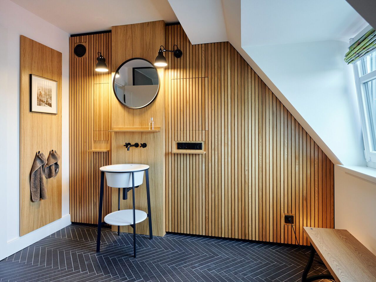 Modernes Badezimmer unter Dachschräge mit Holzverkleidung, rundem Spiegel und minimalistische Waschplatz-Einrichtung.