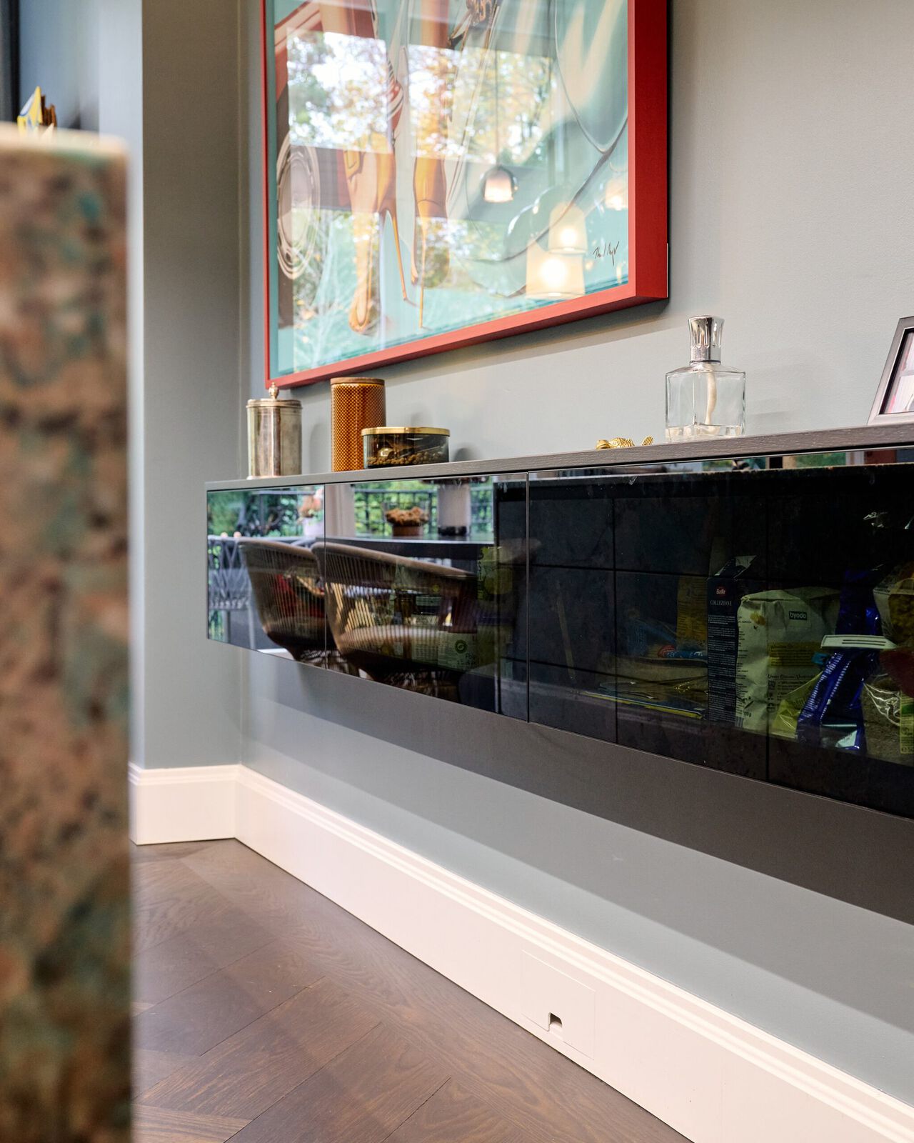 Modernes Wohnzimmer mit schwarzem Sideboard unter einem roten Wandbild und weißer Wandpaneele.