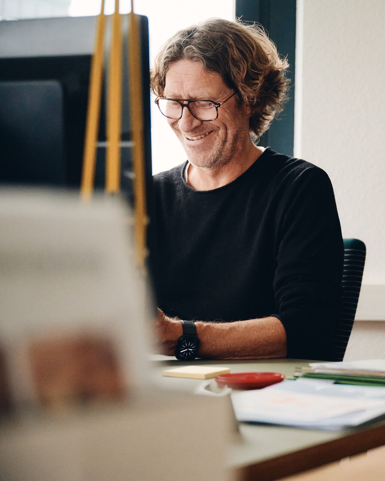 Marc sitzt an einem Schreibtisch in einer Werkstatt und lächelt.