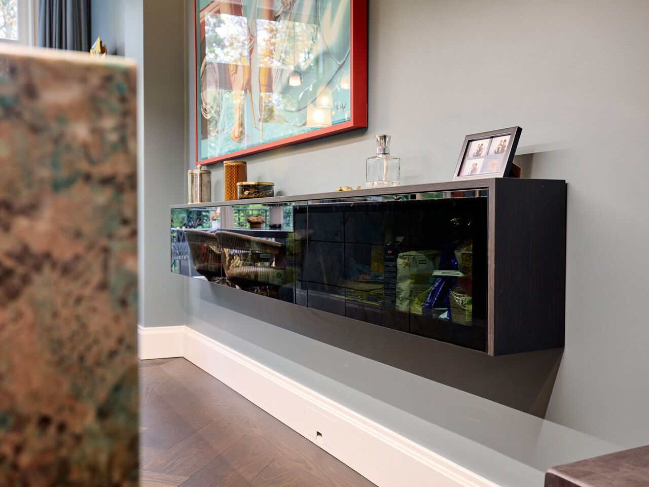 Modernes schwarzes Sideboard an der Wand mit Glast&uuml;ren, darauf Accessoires und ein Tablet, oben ein rotes Gem&auml;lde.