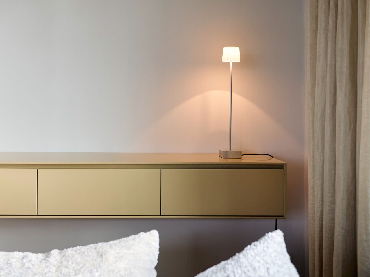 Minimalistisches Schlafzimmer mit beigem Wandpaneel, wei&szlig;en Kissen und schlanker Stehlampe.