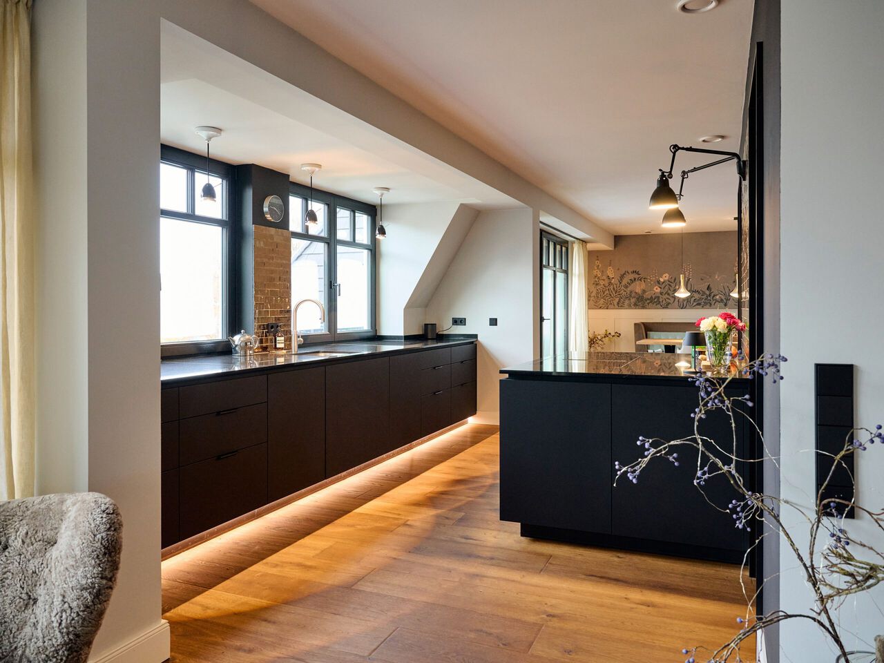 Moderne K&uuml;che mit schwarzen Unterschr&auml;nken, Holzboden und gro&szlig;em Fenster in Dachgeschoss.